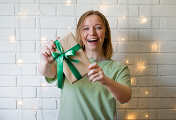 happy young woman holding a gift box over white brick background