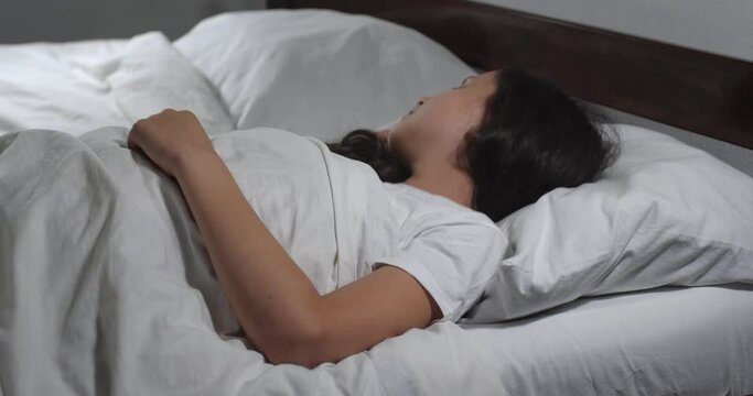 Close up   of  girl 9 years old with long brown hair sleeping  in bed with white linens in light room.  Insomnia concept 4k. Teenager having restless sleep