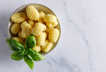 Homemade italian gnocchi. Fresh homemade uncooked gnocchi Italian dumplings on a floured wooden board in a kitchen with fresh basil,potatoes and wheat flour behind .