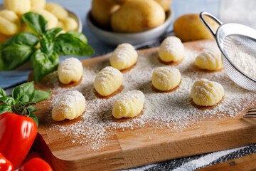 Homemade italian gnocchi. Fresh homemade uncooked gnocchi Italian dumplings on a floured wooden board in a kitchen with fresh basil,potatoes and wheat flour behind .