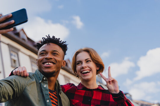 Low angle view of young biracial couple making selfie for soial networks outdoors in town.