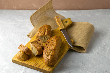 two fresh rye buns on a cutting wooden board and a piece of burlap one of the buns is cut there is a knife next to it