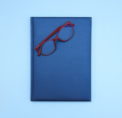 Close up view of isolated blue hard cover notebook with red glasses on top. Copy space 