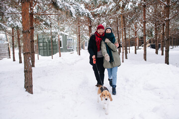 Happy couple hug walking on a snowy pathway with their dog through the yard