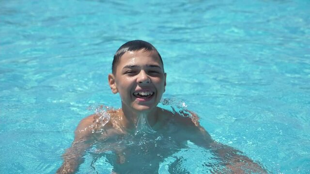 Happy boy smiling and jumping in a swimming pool with clean water in slow motion  
