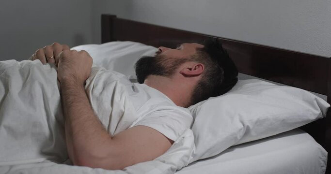Close up of handsome bearded guy waking up in bed with white linens in light room.  Man  getting out of bed fast like being late. Good morning, weekend, leisure, lazy 4k 