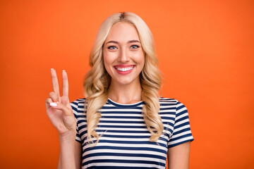 Portrait of attractive cheerful glad wavy-haired girl showing v-sign good mood isolated over bright orange color background