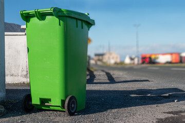 Green plastic wheelie bin in a street ready for collection, waste and recycle industry. Warm sunny day. Low angle of view, selective focus