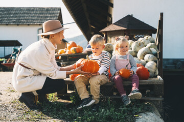 Mother with children are choosing pumpkin in farm market. Woman and little kids playing on fall...