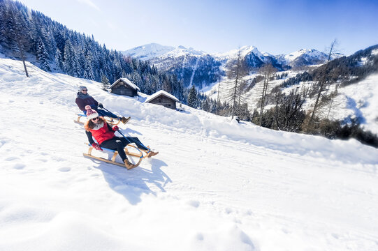 Playful couple sledding on snow during winter
