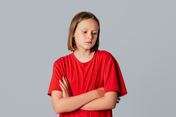 Young pretty girl with crossed arms looks away like she is very disappointed, very sad or doesn't want to hear anything, dressed in casual red t shirt. Young emotional woman