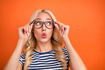 Portrait of attractive amazed pretty girl touching specs looking aside copy space isolated over bright orange color background
