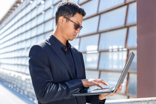 Male Professional Typing On Laptop While Standing Outside Office Building