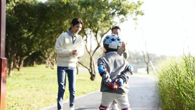 little asian boy learning roller skating encouraged by parents 