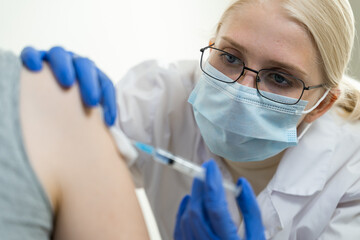Young woman doctor vaccinates a patient in the shoulder. Vaccination against coronavirus or...