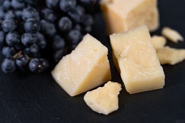 Delicious Parmesan cheese and a bunch of fresh black grapes lie on the table. Wine appetizer. Close-up, top view.