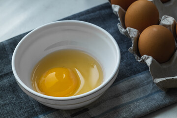 Broken chicken egg in a white plate near a chicken box on a gray napkin.