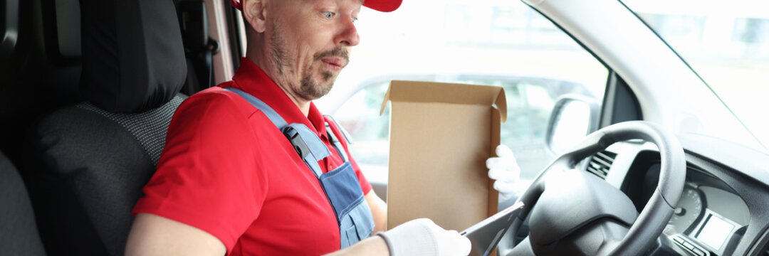 Surprised male courier taking digital tablet out of cardboard box