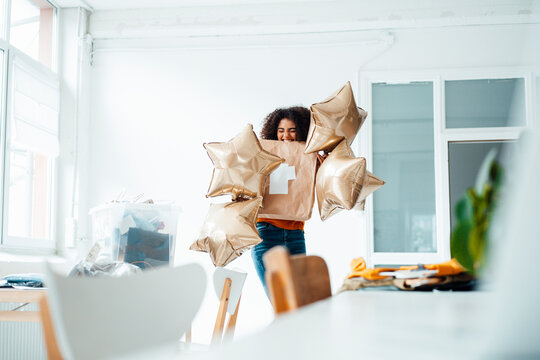 Cheerful woman with eyes closed holding star balloons at home