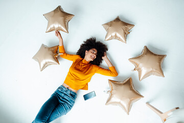 Smiling woman amidst star balloons lying on floor at home