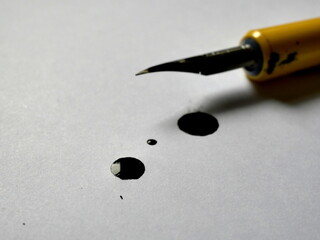 Drawing pen with nib, black from ink with a drop of ink on a white paper