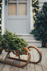 Door of wooden house decorated with festive lights and Chrismas wreath. Sled with pine. Holiday house decoration.