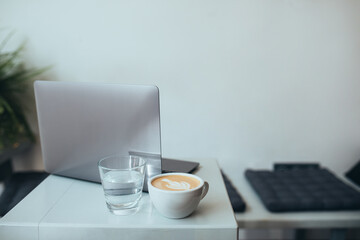 Cup with fresh coffee cappuccino and laptop on a white table.