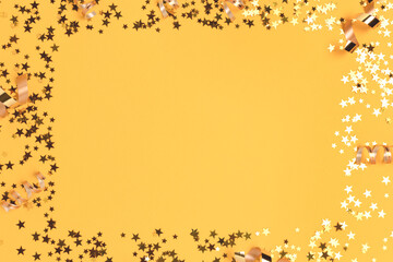Border frame made of gold colored confetti on a yellow background.
