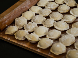 Fototapeta na wymiar Raw Russian dumplings on a cutting board. Homemade dumplings on a black background. The process of preparing meat dumplings, ravioli.