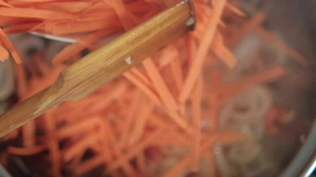 Adding spoon of grated yam and carrots to pot with onion and tomato slices