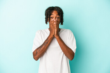 Young african american man isolated on blue background covering mouth with hands looking worried.