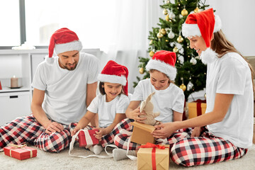 Fototapeta premium family, winter holidays and people concept - happy mother, father and two daughters in santa hats opening christmas gifts at home