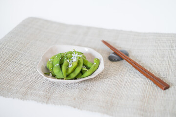 Green pea pods on white plate with wooden chopsticks on mat in Japanese restaurant, close-up