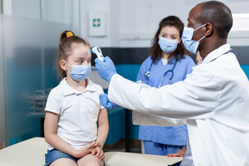 African american pediatrician doctor with face mask against coronavirus measuring girl temperature...