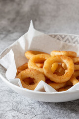 Battered onion rings in a dish,  with paper towel to absorb grease and oil.  On a concrete background