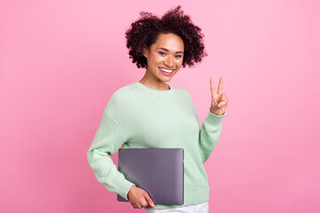 Photo of funny pretty dark skin lady hold netbook fingers show v-sign isolated on pink color...