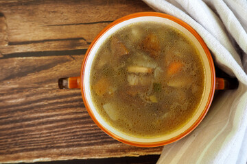 mushroom soup with Polish mushrooms, carrots, potatoes and onions in a brown plate stands on a wooden table next to a beige towel. top view
