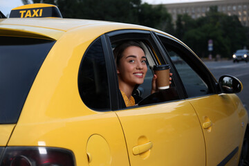 Beautiful young woman with cup of coffee in taxi outdoors