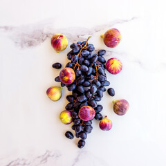 A composition of dark blue grapes and ripe figs on a white stone table. Concept-  healthy diet, vegetarianism, Mediterranean diet.