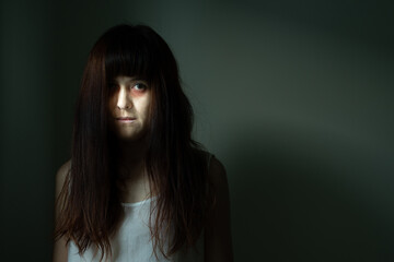 Female ghost in white dress in room. A young scary girl in an old white dress staring in to the camera ferociously with dark background. Asian woman make up ghost face at house. Scary horror concept.