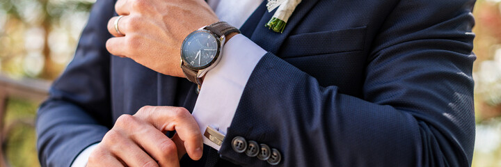 Groom fixing his cufflinks. Handsome groom dressed in dark blue formal suit getting ready for...