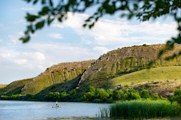 
A man on a SUP on the river in summer at sunset against the background of mountains Two sisters