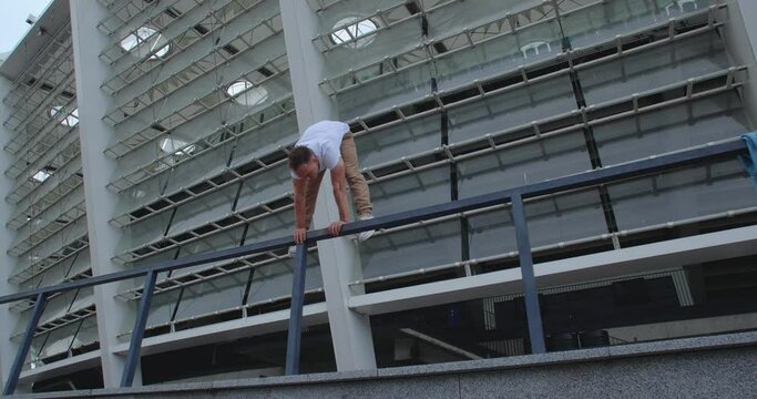 Professional acrobat performing dangerous trick on the railings against backdrop of modern stadium. Caucasian guy  making a handstand with straddle split on a narrow metal pipe
50 fps slow motion
