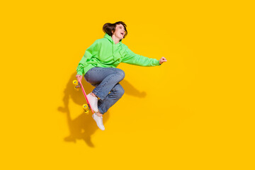 Fototapeta na wymiar Full length body size view of attractive cheerful girl jumping riding skate isolated over bright yellow color background