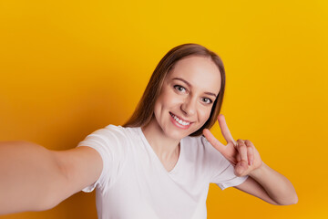 Photo of young girl good mood shoot selfie show peace cool v-sign isolated on vivid yellow colored background