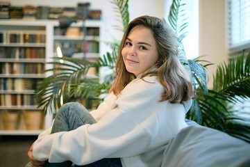 Young teenager girl sits at home on sofa and smiling. Portrait of an ordinary girl