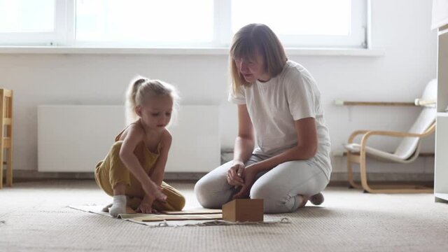 teacher mom and kid toddler girl playing with natural wooden toys on floor in bright room, classes with montessori materials and educational toys, rough tablets, sensory development