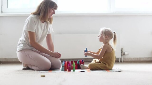 teacher mom and child toddler girl playing with natural wooden toys on floor in a bright room, classes with montessori materials and educational toys, rough tablets, sensory development