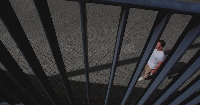  Caucasian guy in beige trousers and white T-shirt on the sidewalk walk behind the metal parapet on the street of the city
50 fps slow motion