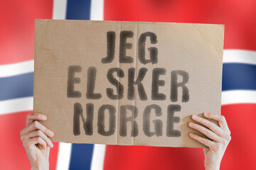 The phrase " Jeg elsker Norge " on a banner in men's hand with blurred Norwegian flag on the background. Love. Patriotic. Patriotism. Destination. Northern Europe